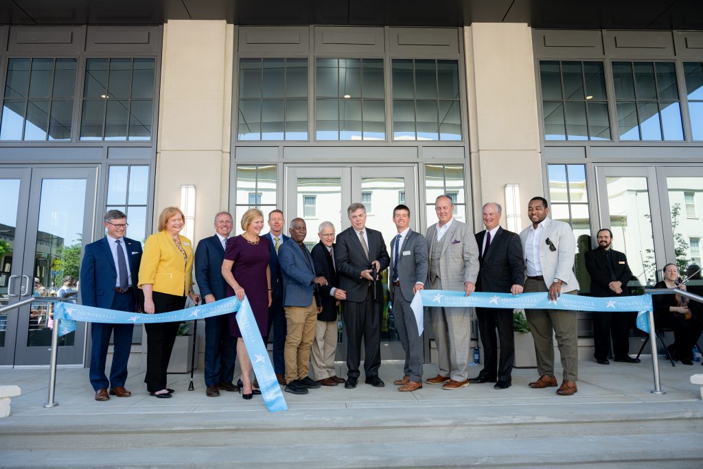 Mayor Tommy Battle, center, cuts the ribbon on the new city hall on Tuesday, May 21, 2024. He is joined by members of the Huntsville City Council and other city officials. The ribbon is blue. They are in front of the building.
