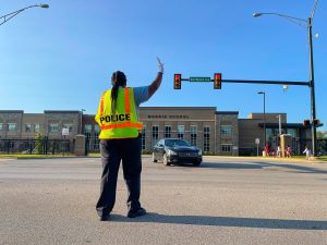 Female in safety vest directing traffic at an intersection outside a school.