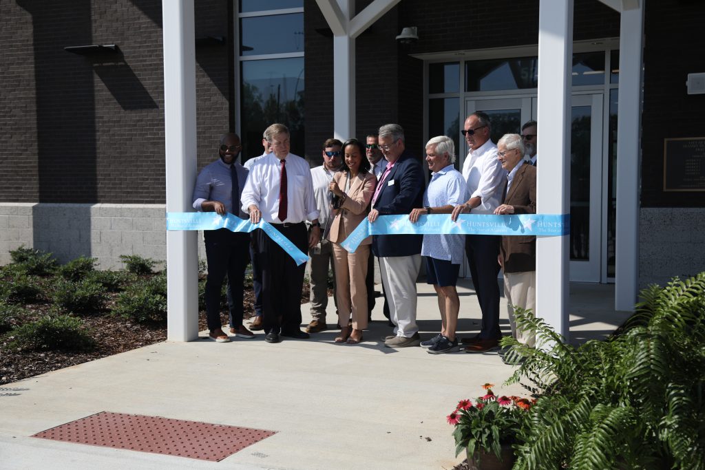 Group of people cutting a ribbon outside a brick building