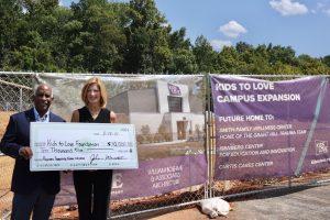 man and woman holding oversized check in front of construction fence with banner