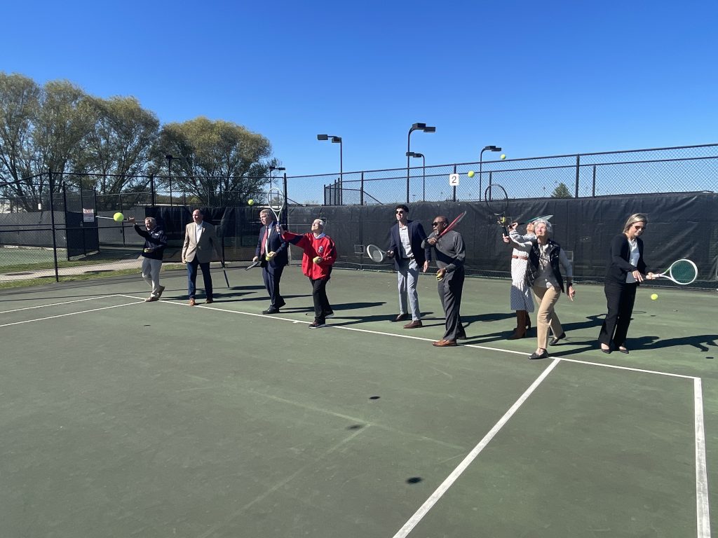 Group of people on tennis court hitting tennis balls all at once with blue sky in background