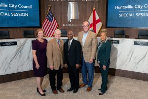 two women and three men pose together for photo with flags in background