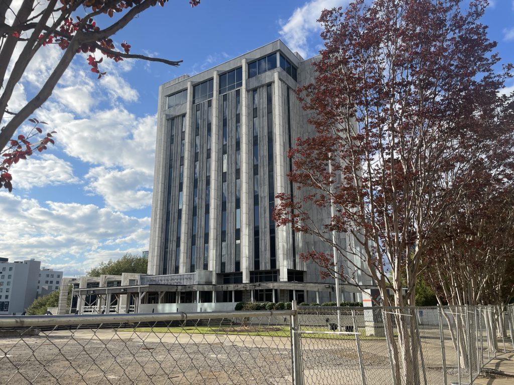 tall, gray colored building with windows and small tree onthe right