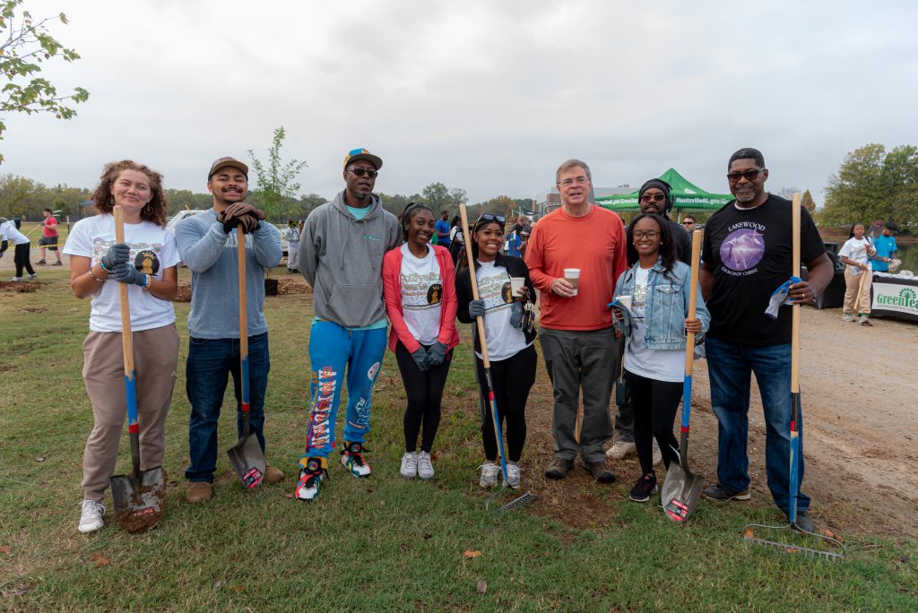 group of people, some holding shovels, standing in grassy field