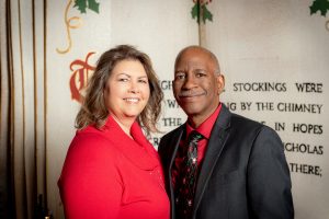 woman in red shirt on left, man in dark coat on right with Christmas background