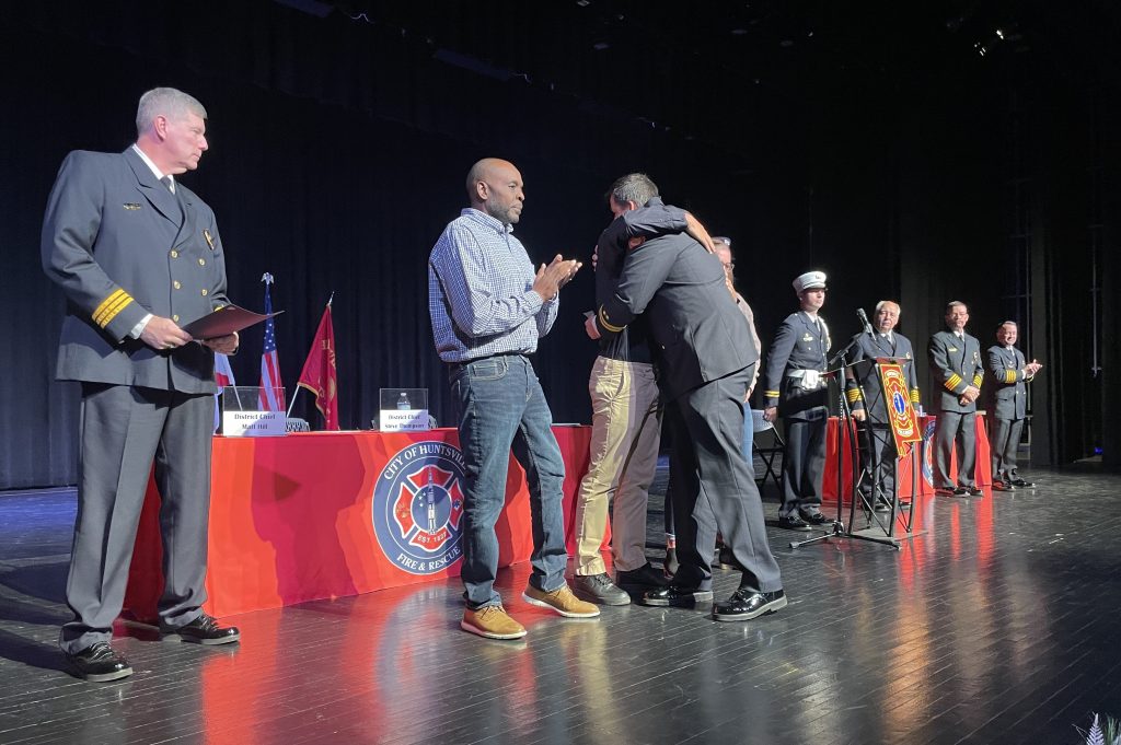 Two men hug as two men look on in ceremony on stage