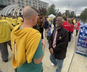 Two men talking on concrete walkway with other people in background