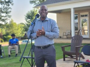 man in blue shirt stands behind microphone in outdoor setting